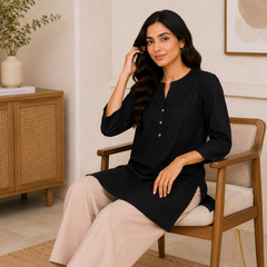 Woman sitting on a chair wearing a black top and beige pants in a home setting.