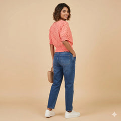 Woman wearing a pink top and blue jeans against a beige background