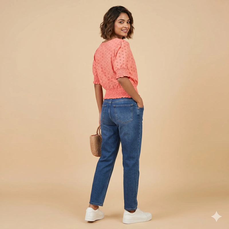 Woman wearing a pink top and blue jeans against a beige background
