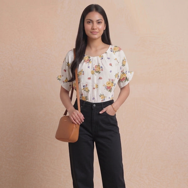 Woman wearing a floral blouse and black pants with a brown handbag on a beige background