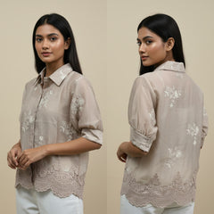Woman wearing a beige floral embroidered shirt against a beige background