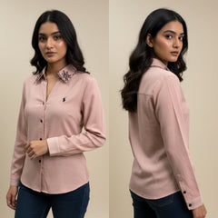 Woman wearing a pink shirt with a floral collar detail, standing against a beige background.