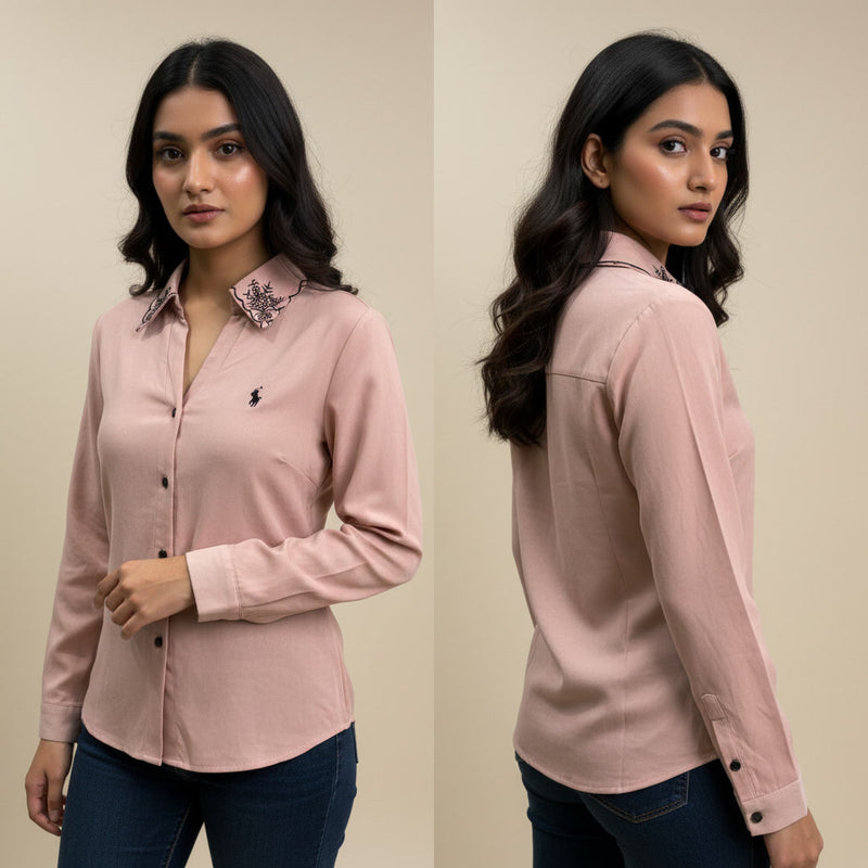 Woman wearing a pink shirt with a floral collar detail, standing against a beige background.