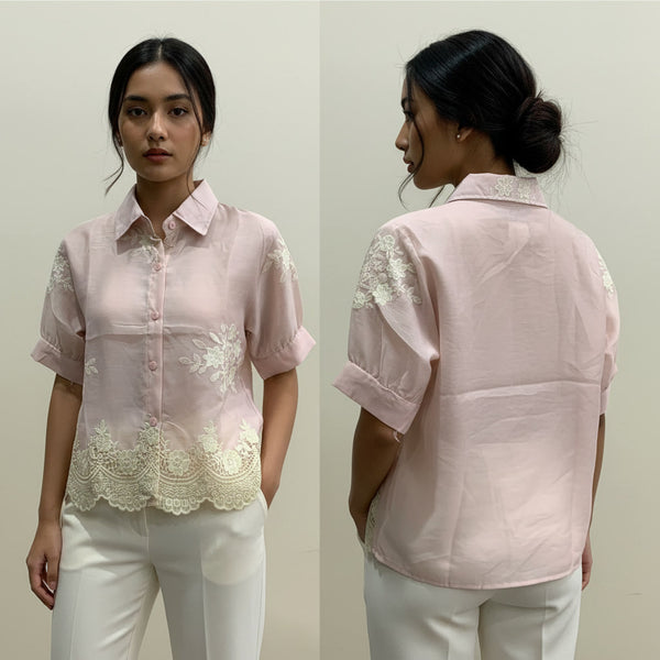 Woman wearing a light pink blouse with lace details on a plain background