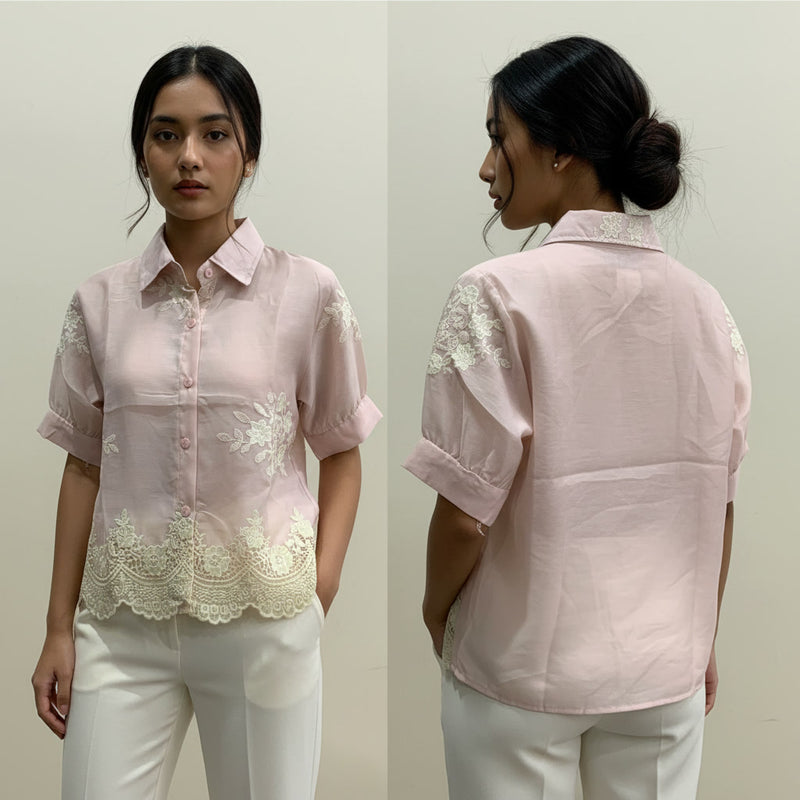 Woman wearing a light pink blouse with lace details on a plain background
