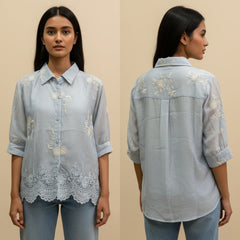 Woman wearing a light blue embroidered shirt from front and back views on a beige background