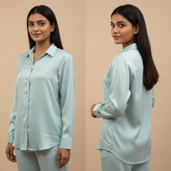 Woman wearing a light blue shirt and pants set, standing against a beige background.