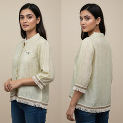 Woman wearing a light green textured shirt with fringes on a beige background