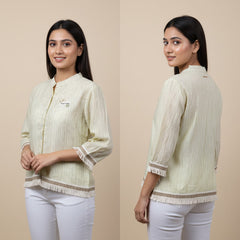 Woman wearing a light-colored blouse with lace details, standing against a beige background.