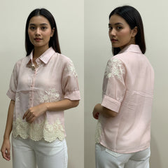 Woman wearing a light pink blouse with lace details on a plain background