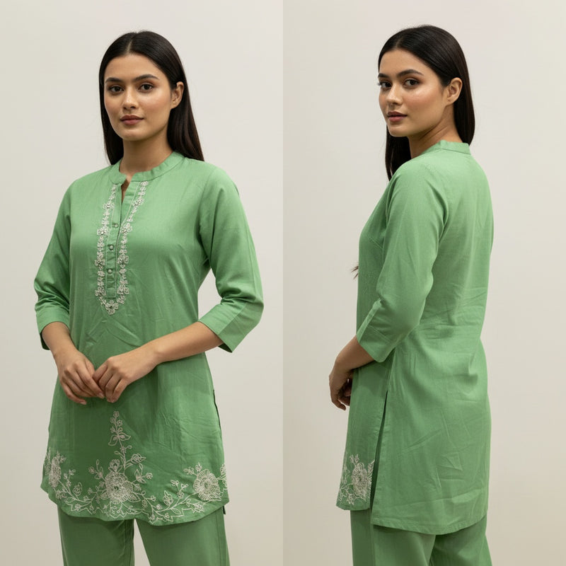 Woman wearing a green traditional outfit with embroidery on a plain background