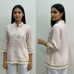 Woman wearing a light-colored striped shirt with a brand logo, standing against a plain background.