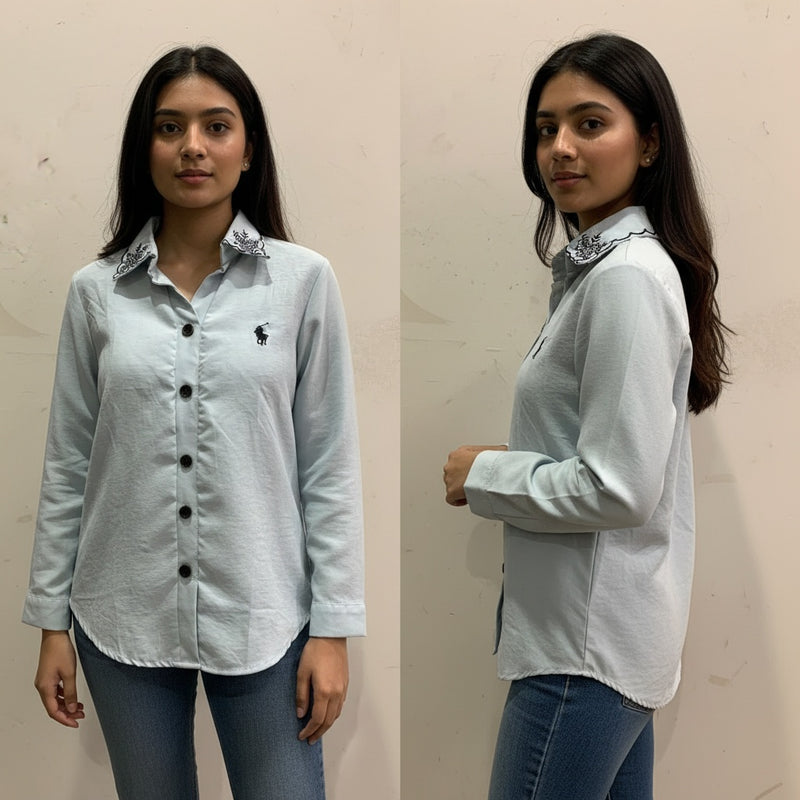 Woman wearing a light blue shirt with a collar design, standing against a plain background.