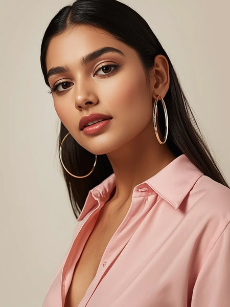 Woman wearing a pink shirt with hoop earrings against a beige background