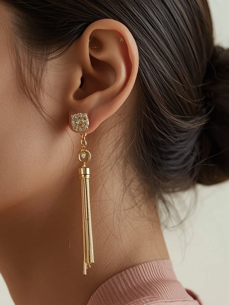Close-up of a woman wearing gold earrings with tassels on a neutral background