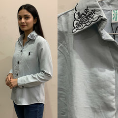 Woman wearing a light gray shirt with floral embroidery on a beige background