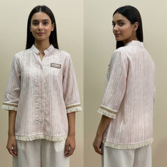 Woman wearing a light pink and white striped shirt with a brand logo, standing against a beige background.