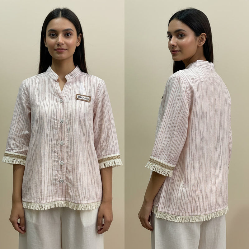 Woman wearing a light pink and white striped shirt with a brand logo, standing against a beige background.