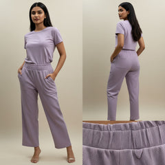 Woman wearing a lavender outfit with matching pants and top on a beige background.