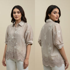 Woman wearing a beige embroidered shirt with a plain background