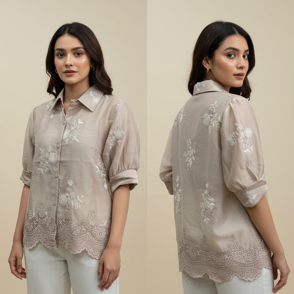 Woman wearing a beige embroidered shirt with a plain background