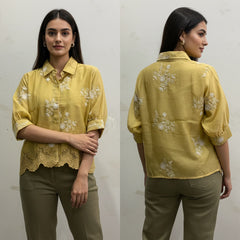 Woman wearing a yellow floral blouse with lace details, standing against a plain background.